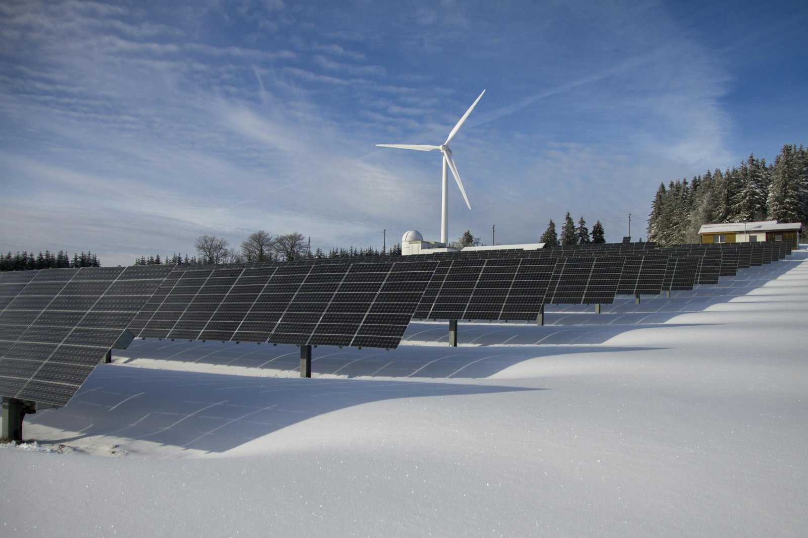 Solar panels and wind turbine in a snowy landscape, showcasing renewable energy sources.