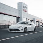 Stylish modern white car parked in front of a Toyota dealership showroom.