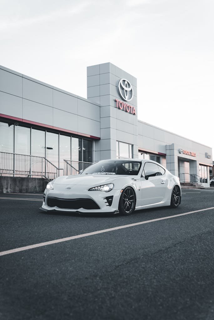 Stylish modern white car parked in front of a Toyota dealership showroom.