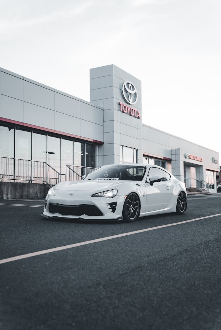 Stylish modern white car parked in front of a Toyota dealership showroom.