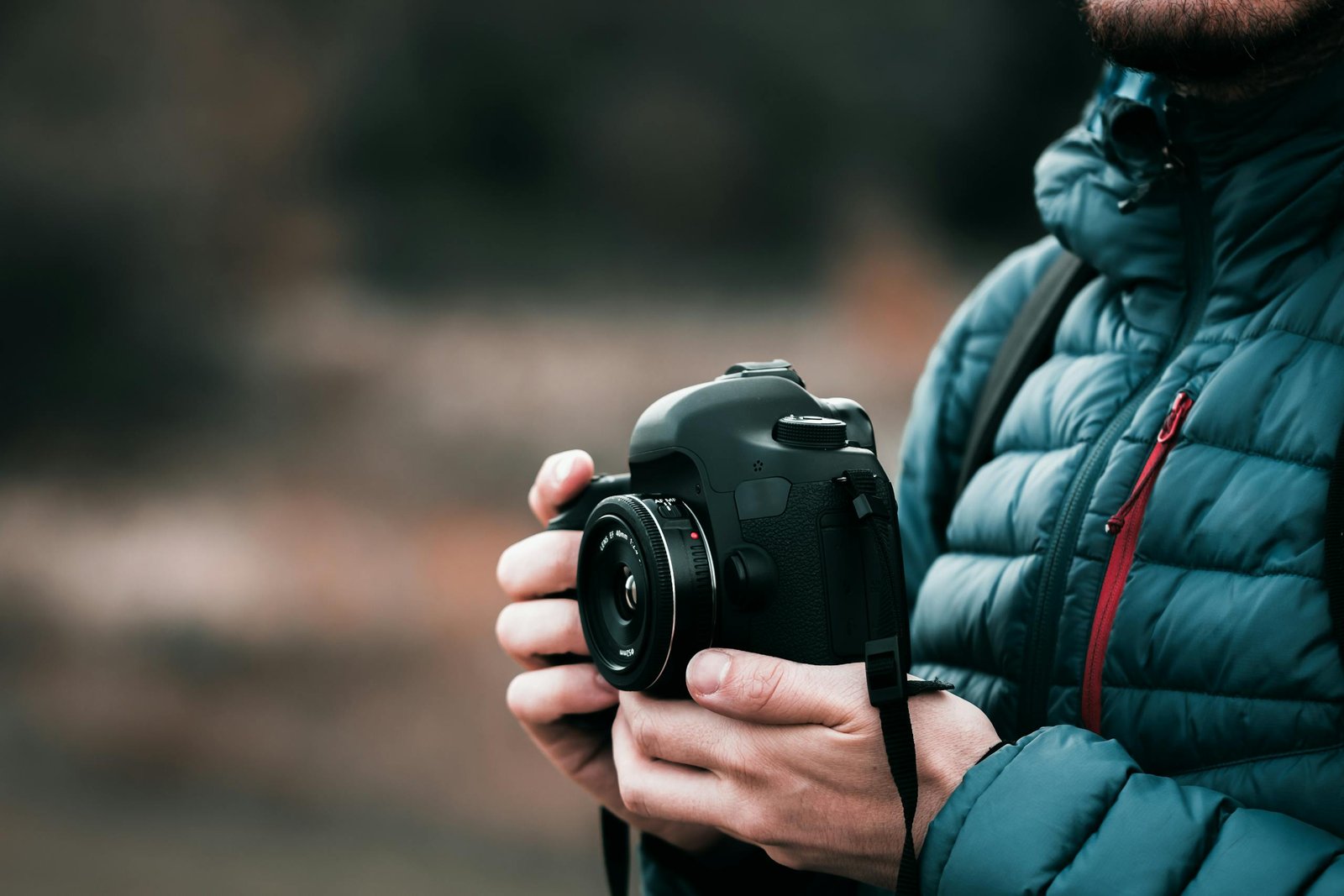 Close-up image of a photographer holding a DSLR camera outdoors in a puffer jacket, showcasing focus and creativity.