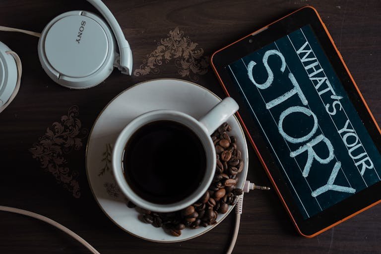 Flat lay of coffee cup, headphones, and tablet with 'What's Your Story' on screen.